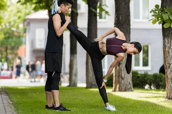 Aziatische Sportman Helpen Vrouwelijke Atleet Rekken Gras Park — Gratis stockfoto