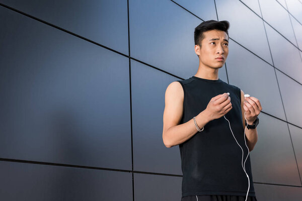 Young asian sportsman putting on earphones at city street — Stock Image Young Asian Sportsman Putting Earphones City Street Stock Picture