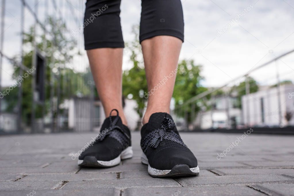 cropped image of sportswoman legs in black sneakers standing at street