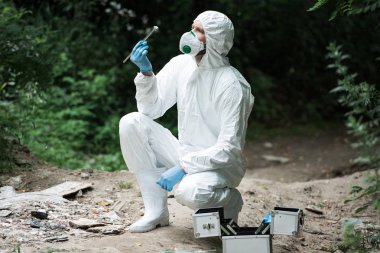 cımbız ormandaki tarafından tutarken taş inceleyerek maske ve koruyucu giysi içinde erkek bilim adamı odaklı 