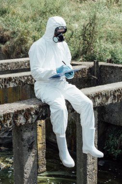 seçici odak koruyucu maske ve kanalizasyon yakınındaki otururken Pano'da yazma takım elbise erkek bilim adamı 