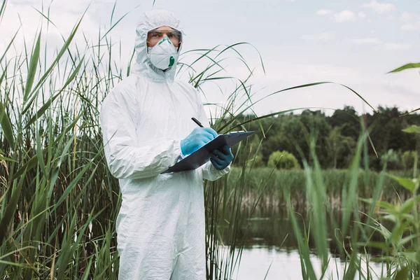 Ernsthafte Männliche Wissenschaftler Schutzmaske Und Anzug Schreiben Klemmbrett Der Nähe — Stockfoto