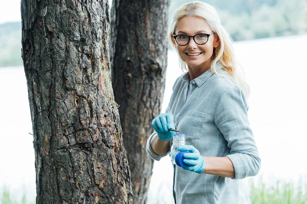 Sonriente Científica Gafas Poniendo Muestra Corteza Árbol Por Pinzas Frasco — Foto de stock gratuita