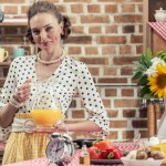 Smiling adult housewife holding jug of orange juice and looking at camera at kitchen