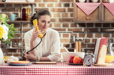 Retro kablolu telefonla konuşurken ve uzak mutfak seyir yetişkin ev kadını gülümseyen