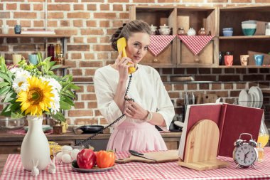 telefonla konuşurken ve mutfakta yemek hazırlama sırasında kameraya bakıyor güzel yetişkin ev hanımı