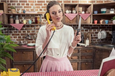 Mutfak sarı kablolu telefonla konuşurken bıçak ile ciddi yetişkin ev kadını