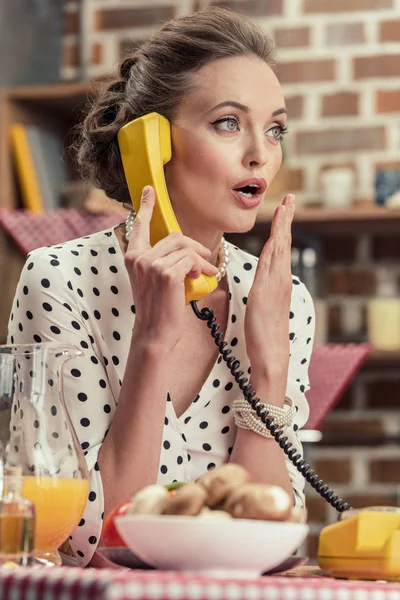 shocked adult housewife talking by vintage wired phone at kitchen