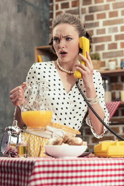 confused adult housewife talking by vintage wired phone at kitchen