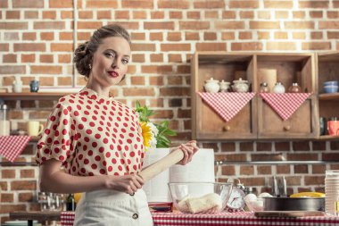ciddi yetişkin ev kadını oklava tutarak ve mutfak kameraya bakarak vintage giyim