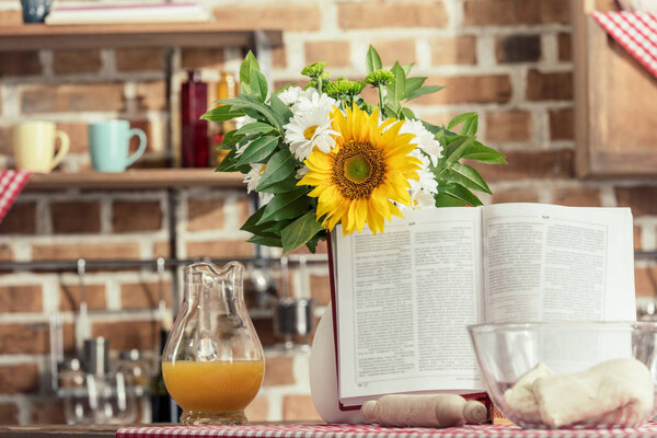 recipe book and bouquet of flowers on cooking table at kitchen