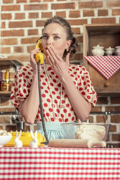 shocked adult housewife talking by vintage phone at kitchen