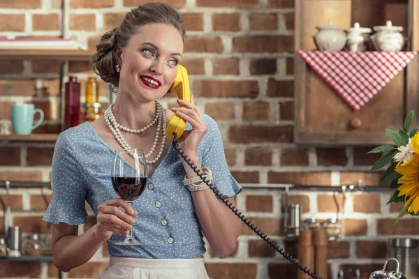 有吸引力的成人家庭主妇用葡萄酒的酒杯交谈在厨房的老式旋转电话 — 免费的图库照片