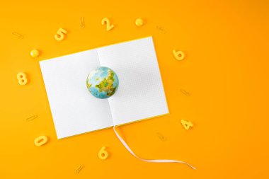 top view of earth globe on blank notebook surrounded with digits and paper clips on yellow clipart