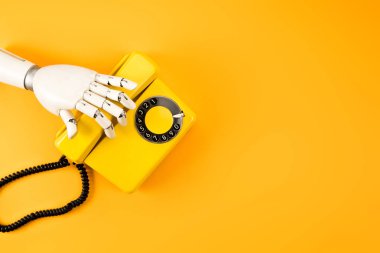 cropped shot of robotic hand reaching for vintage phone on yellow tabletop clipart