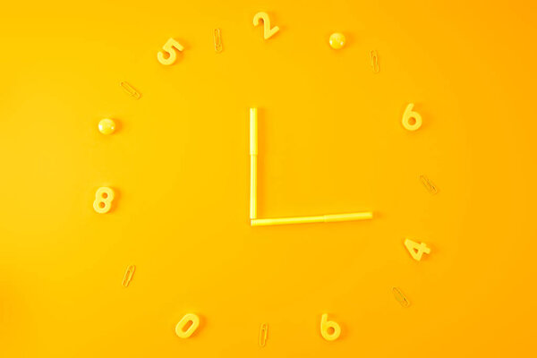 вид сверху на часы из маркеров, пластиковых цифр и скрепки на желтом
