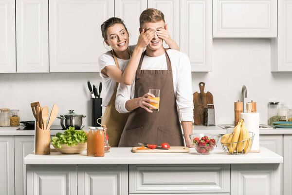 girlfriend closing eyes for boyfriend while he cooking salad in kitchen