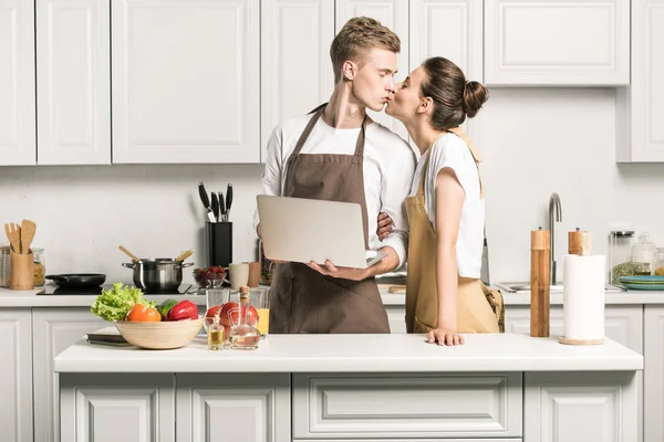 Young Couple Kissing Kitchen Holding Laptop — Stock Photo, Image