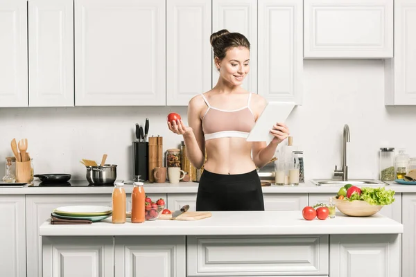 有吸引力的女孩运动胸罩阅读食谱烹饪在厨房片剂 — 图库照片