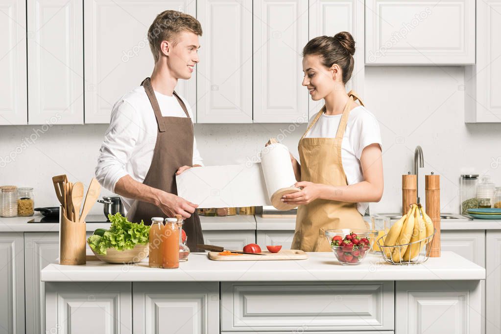 young couple cooking salad and holding paper towel in kitchen