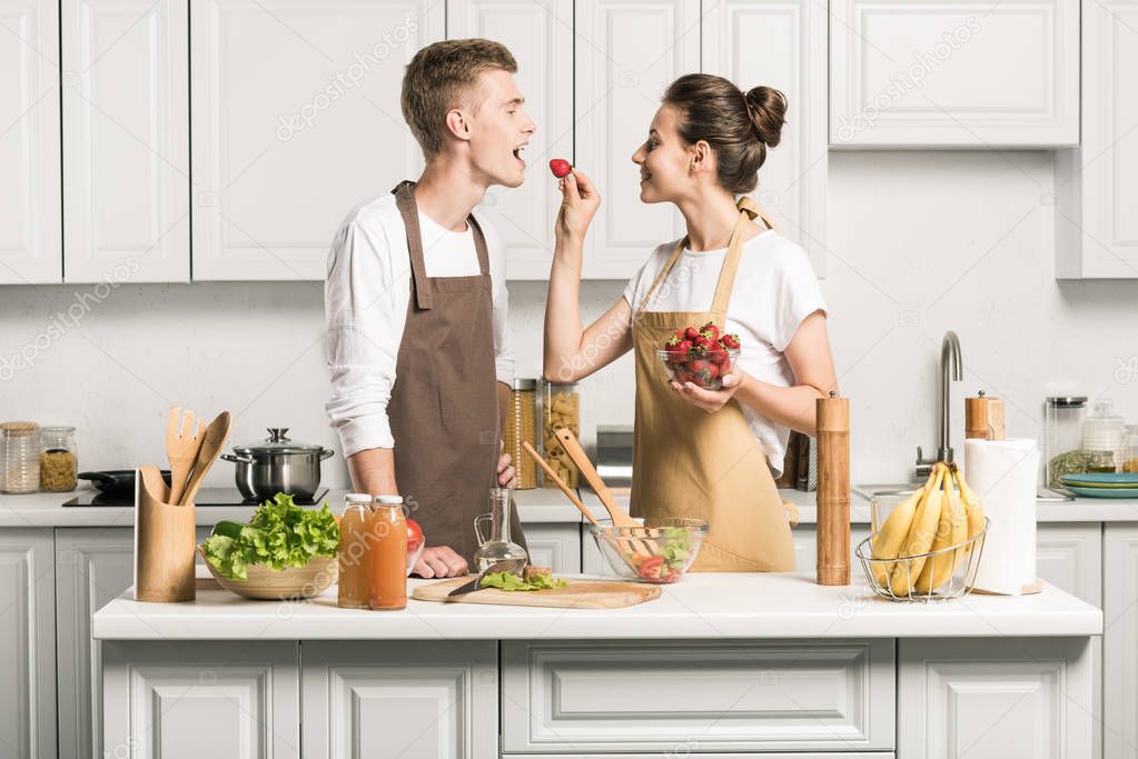 girlfriend feeding boyfriend with strawberry in kitchen