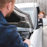 Father repairing car with open hood, son waving hand