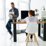 Father writing to notebook, son using computer at home