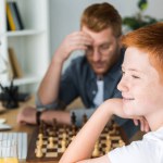 Zamyślony ojciec i syn gra w szachy w domu