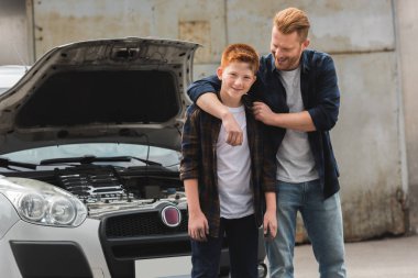 father hugging son after repairing car with open hood clipart