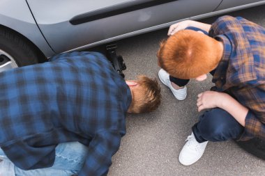 high angle view of father and son lifting car with floor jack for changing tire clipart