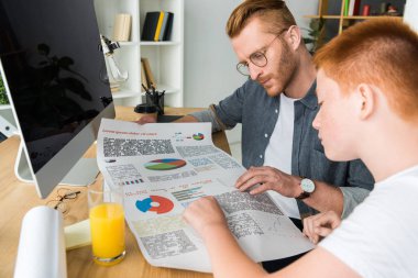 father and son looking at diagram at table at home clipart