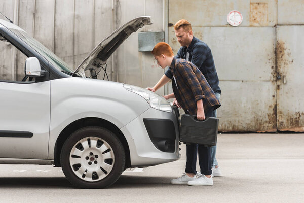 side view of father and son repairing car with open hood together