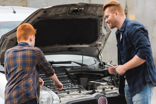 ginger hair father and son repairing car with open hood