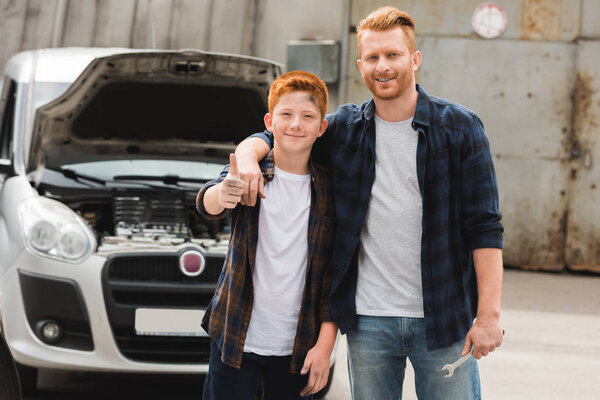 father hugging son after repairing car and he showing thumb up