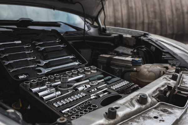 broken car with open hood on street, box with tools