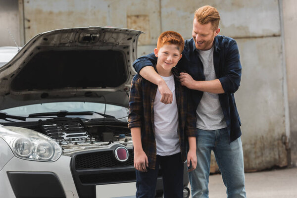 father hugging son after repairing car with open hood