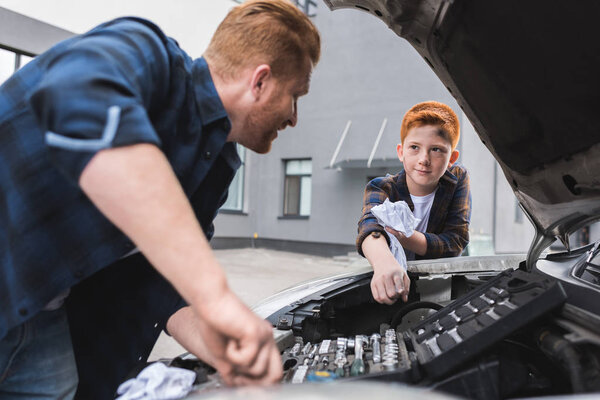 father repairing car with open hood, son pointing on something