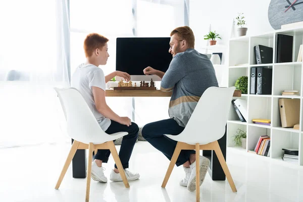 아버지와 아들이 집에서 컴퓨터와 테이블에서 체스를 — 스톡 사진