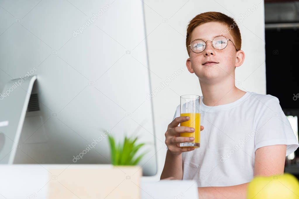 preteen ginger hair boy holding glass of juice at home