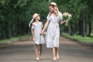 Anne ve kızı elele ve yeşil Park'ta yürüyordunuz hasır şapkalar