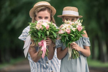 mutlu anne ve kızı hasır şapka ile çiçek buketleri yüzleri önünde poz içinde