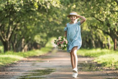 pretty female child in dress and straw hat holding bouquet of flowers and walking in garden clipart