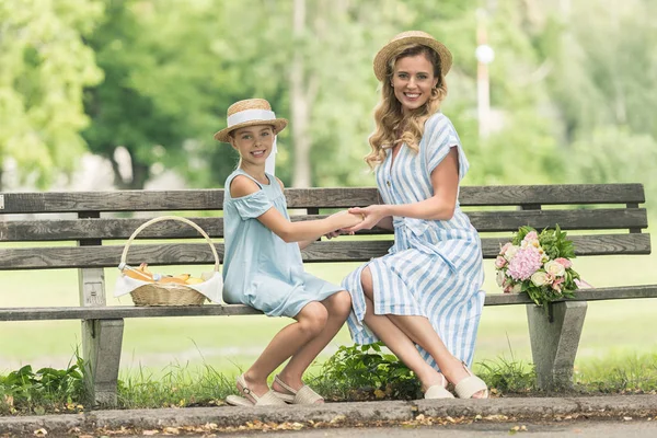 美丽的父母和微笑的女儿牵着手 坐在长凳上 柳条篮和花束 — 免费的图库照片