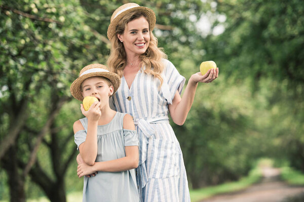 beautiful mother and daughter eating appples in green garden 