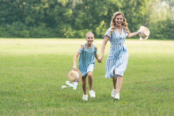 beautiful mom and daughter holding hands and running on green lawn
