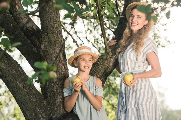 Szczęśliwa Matka Córka Słomkowe Kapelusze Trzymając Jablka Stojący Pobliżu Drzewa — Zdjęcie stockowe