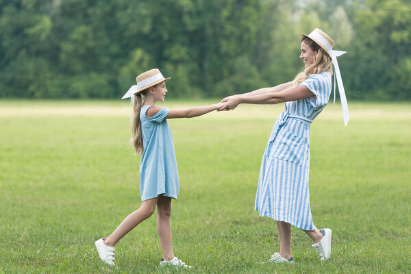 happy mother and adorable daughter holding hands and twisting on green lawn