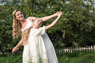 neşeli anne ve kızı beyaz elbiseler bahçede elele