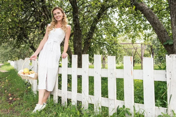 Elegancka Kobieta Owocami Wiklinowy Kosz Stojący Pobliżu Biały Płot Ogrodzie — Zdjęcie stockowe