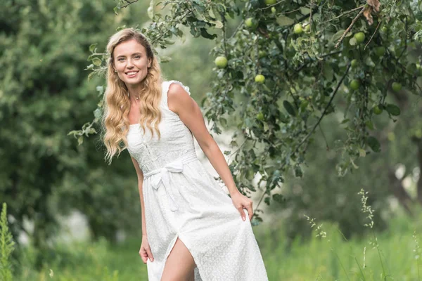 Όμορφη Χαμογελαστή Γυναίκα Στην Λευκή Φόρεμα Θέτοντας Περιβόλι Δέντρα Μηλιάς — Φωτογραφία Αρχείου
